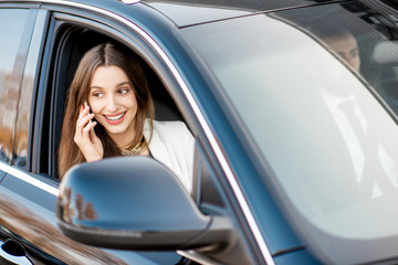 Obraz na płótnie Canvas Elegant businesswoman talking with phone driving luxury car with businessman in the city, view from the outside through the window
