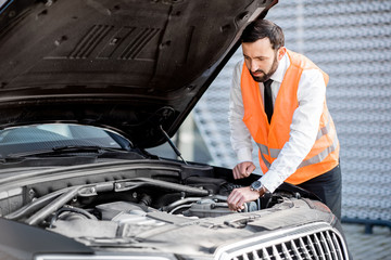 Businessman in waistcoat looking to the engine of his broken car on the road