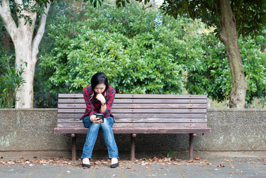 公園のベンチでスマートフォンを操作する女性