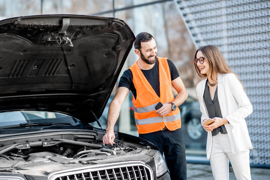 Handsome service worker consulting or providing technical assistance of the broken car to the businesswoman outdoors