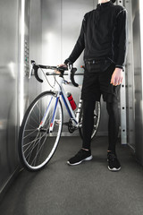 Obraz premium Sports young man stands with a bicycle in the elevator. Close-up photo of foot and bike.