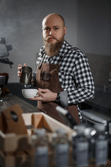 Brutal young barista in an apron makes coffee at the bar in a modern cafe