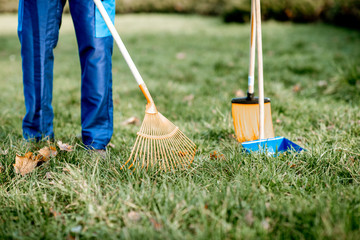 Man sweeping leaves with orange rake on the green lawn, close-up view with no face