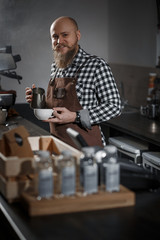 Brutal young barista in an apron makes coffee at the bar in a modern cafe