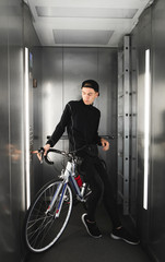 Portrait of a young man riding in the elevator along with a bicycle. Cyclist drops a bicycle in the elevator on the first floor. © bodnarphoto