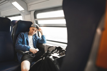 Young man sleeping in a train near the window with headphones and a smartphone in his hands. The...