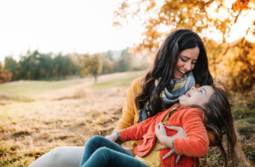 A portrait of young mother with a small daughter in autumn nature at sunset.