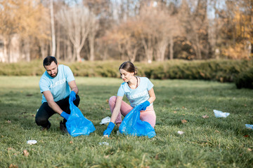Happy man and woman volunteers dressed in blue t-shirts cleaning public garden from plastic rubbish...