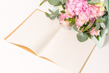 Floral mock-up and empty space for text. Bouquet of pink flowers. Open vintage craft notebook or diary with tender flowers decoration on the white table.