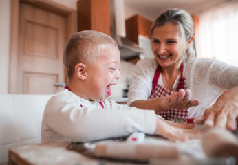 A laughing handicapped down syndrome child with his mother indoors baking.
