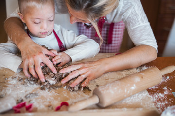 A happy handicapped down syndrome child with his mother indoors baking.