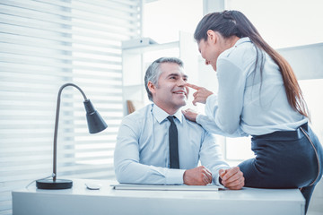 Smiling boss. Long-haired beautiful female sitting on the table and flirting with her boss