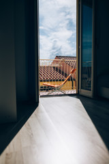 Open window with city roofs view in Italy. Light and shadow in room