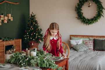 girl burgundy dress decorates Christmas rustic room