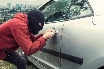 Close up of man in black robber mask breaking the car lock on a city background. Ill-intended thief...