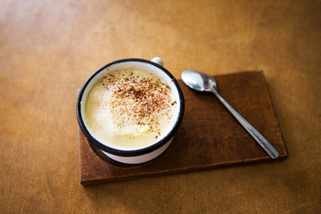 a cup of cappuccino stands on a wooden table and stands for a spoon.