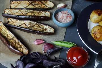Flat lay of delicious dinner table for two with fried eggplants, garlic and tomatoes sause on dark stone background.