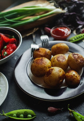 Delicious dinner table for two with fried potatoes, organic tomatoes salad, olives, green onion, eggplants on dark stone background.