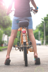 Close up from back side of a girl with bicycle ready to ride on concrete path during sunset or sunrise with blurred background