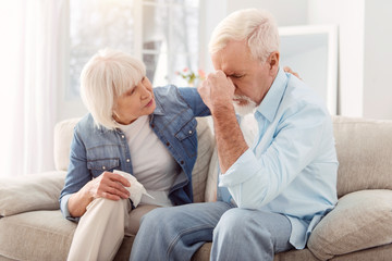 Healthcare. Short-haired aging woman looking thoughtful and worried while sitting next to her husnabd in the apartment