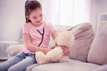 Beaming preschooler. Beaming pleasant preschooler feeling amazing while playing with her teddy bear in living room