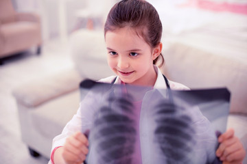 Daughter of doctor. Little cute dark-haired daughter of doctor playing alone with x-ray of lungs