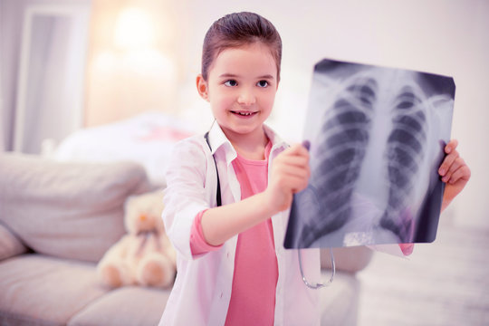 X-ray of lungs. Cute dark-eyed girl wearing white jacket feeling interested while holding x-ray of lungs