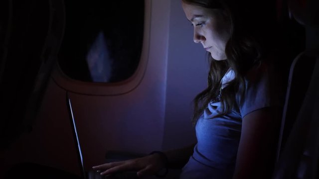 Woman work on notebook in airliner, dark plane salon during nigh flight