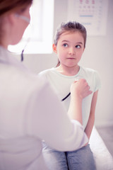 Holding breath. Dark-haired girl holding her breath while family physician listening to her lungs