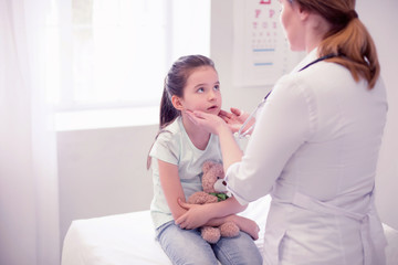 Sore throat. Professional experienced family physician examining little girl having sore throat