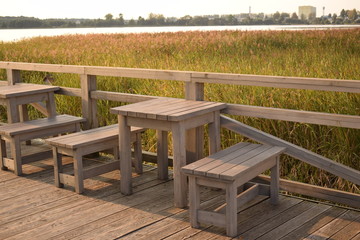 Wooden tables and benches on the lake with reeds waiting for lovers to watch the sunset.