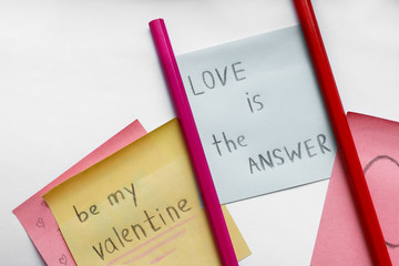 love is the answer, Be My Valentine handwritten inscriptions on the colored stickers and two pencils on the white paper background.