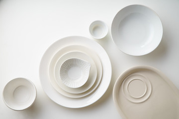 Porcelain plates of various form and size on white background. Overhead image, copy space.