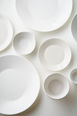 Porcelain plates of various form and size on white background. Overhead image, copy space.