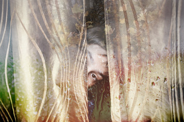 Young boy looks from behind a curtain through a wet window on a rainy day