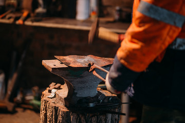Blacksmith workshop. The blacksmith works on the anvil with a hot metal billet