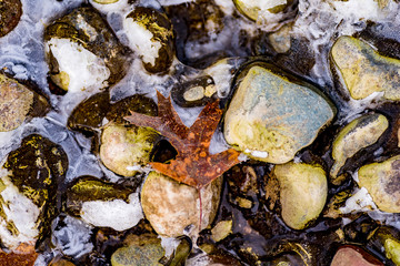 colorful stones and rocks partially frozen in river with snow and frost