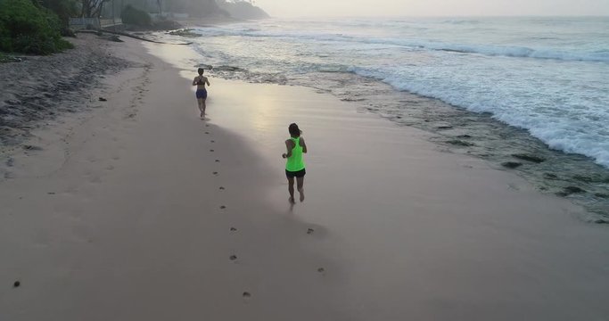 Two healthy lifestyle young women friends running on tropical beach during sunrise in the morning