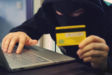 Man in robber mask uses internet, bank account and credit facilities. Phishing attack by male with...