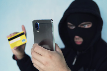 The thief scammer is holding a mobile phone and credit card. The concept of Bank card fraud through...