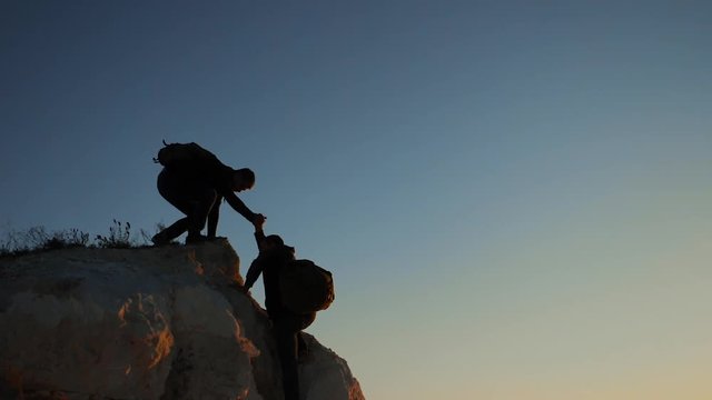silhouette two men teamwork tourists climber climbs a mountain. walking tourist hiking adventure climbers sunset climb the mountain . slow motion video. hiker sunlight on top win victory the hill
