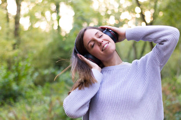 Caucasian european young woman or girl listening to music with helmets relaxed and dancing moving her hair gently in nature or very happy and calm forest