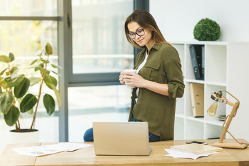 Sunny working day! Elegant and cheerful businesswoman using laptop. Cheerful young beautiful woman in glasses with smile while sitting at her working place.
