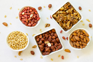 Various nuts in a ceramic bowl (walnut, almonds, pine nuts, hazelnuts) on a light stone table. The concept of a healthy dessert.