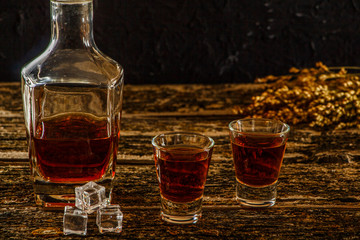 Whiskey with ice or brandy in a glass and a square carafe on an old wooden background. Whiskey with...