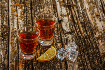 Whiskey with ice or brandy in a glass and a square carafe on an old wooden background. Whiskey with ice in a glass. Whiskey or cognac. Selective focus.