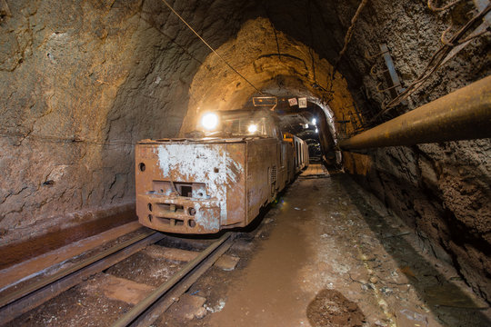 Underground gold iron ore mine shaft tunnel gallery passage with light and electric locomotive loco