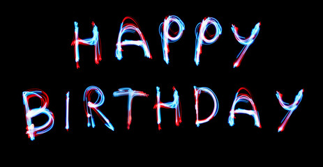 Glowing inscription happy birthday on a black background. blue light image, long exposure with colored fairy lights, against black