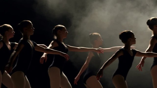 A group of young ballerina girls dancing on stage in the dark, close-up. A large group of children rehearsing and dancing the ballet.