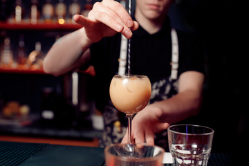 Barman prepares cocktail in transparent glass on bar with alcohol.